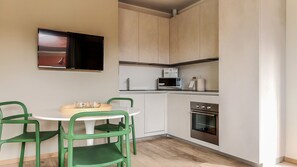 A compact kitchen with a microwave, oven, and a small dining area with two green chairs and a white table.