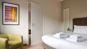 Een hotelkamer met een bed, een groene fauteuil, een deur en een ingelijst schilderij aan de muur.