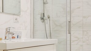 Ein Badezimmer mit weißem Waschbecken, einem Spiegel und einer Dusche inklusive Handbrause.