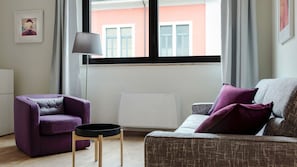 A modern living room with a purple armchair, a grey sofa with purple cushions, a floor lamp, and a radiator.