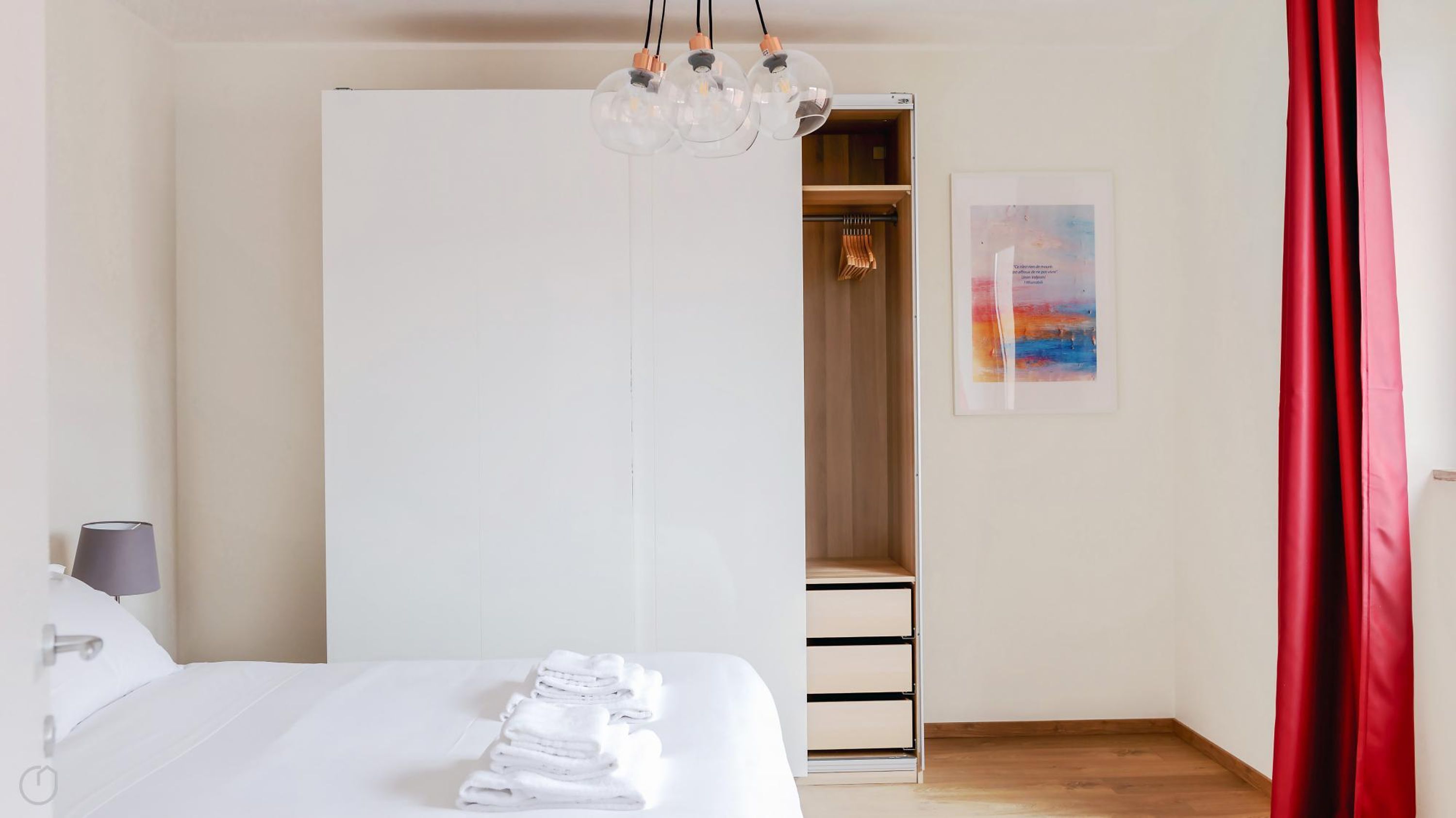 Een hotelkamer met een bed, een kledingkast, een inloopkast, een nachtkastje, een lamp en een schilderij aan de muur.