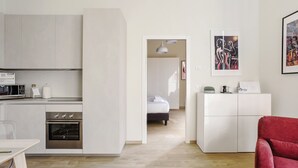 A modern kitchen with built-in appliances, a dining area with a table, and a red chair. A hallway leads to a bedroom with a bed and a nightstand. - Mi-brgz1c1 Bergonzoli Place - Bilo B - Nina (Milan)