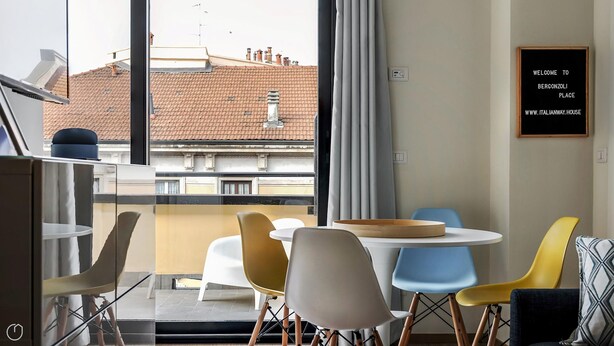 Quarto moderno com mesa de jantar, cadeiras e vista para um telhado de telhas vermelhas.