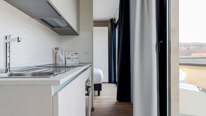 Cozinha moderna com fogão embutido, máquina de café e pequena geladeira. Há uma janela com cortinas e vista para o exterior.