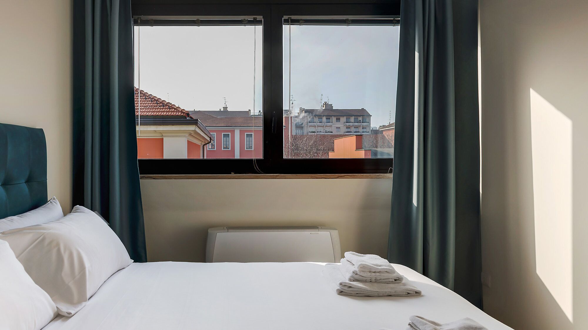 Une chambre d’hôtel avec un lit, une fenêtre avec des rideaux et une vue sur les bâtiments environnants.