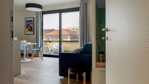 A modern living room with a blue sofa, a dining area with a white table and blue chairs, and a large window with a view of buildings. - Mi-brgz1b4 Bergonzoli Place - Terrace B - On the Grass (Milan)