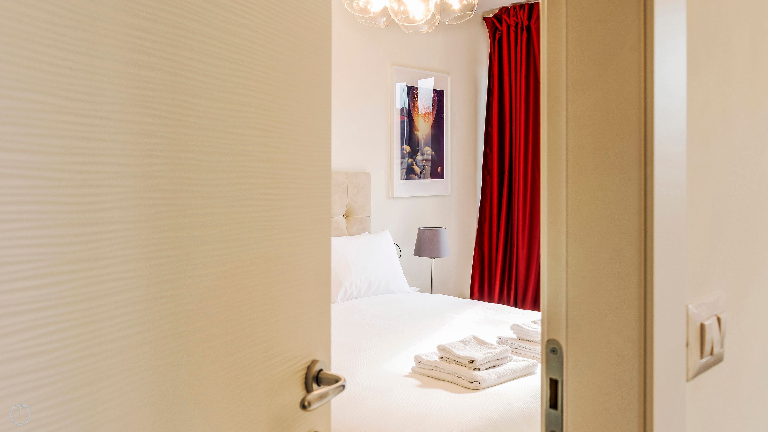 Una habitación de hotel con una cama, una lámpara, una cortina roja y una toalla doblada sobre la cama.