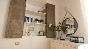 Quarto com cômoda branca, espelho e estantes com livros e plantas.