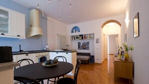 Uma cozinha compacta com armários brancos, uma ilha central e um espaço de refeições com mesa redonda e cadeiras.