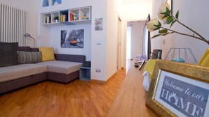 Uma sala de estar moderna com um sofá, uma estante de livros e um letreiro de boas-vindas emoldurado.