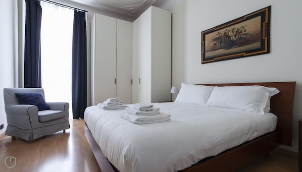A hotel room with a large bed, a chair, a wardrobe, and a painting on the wall.