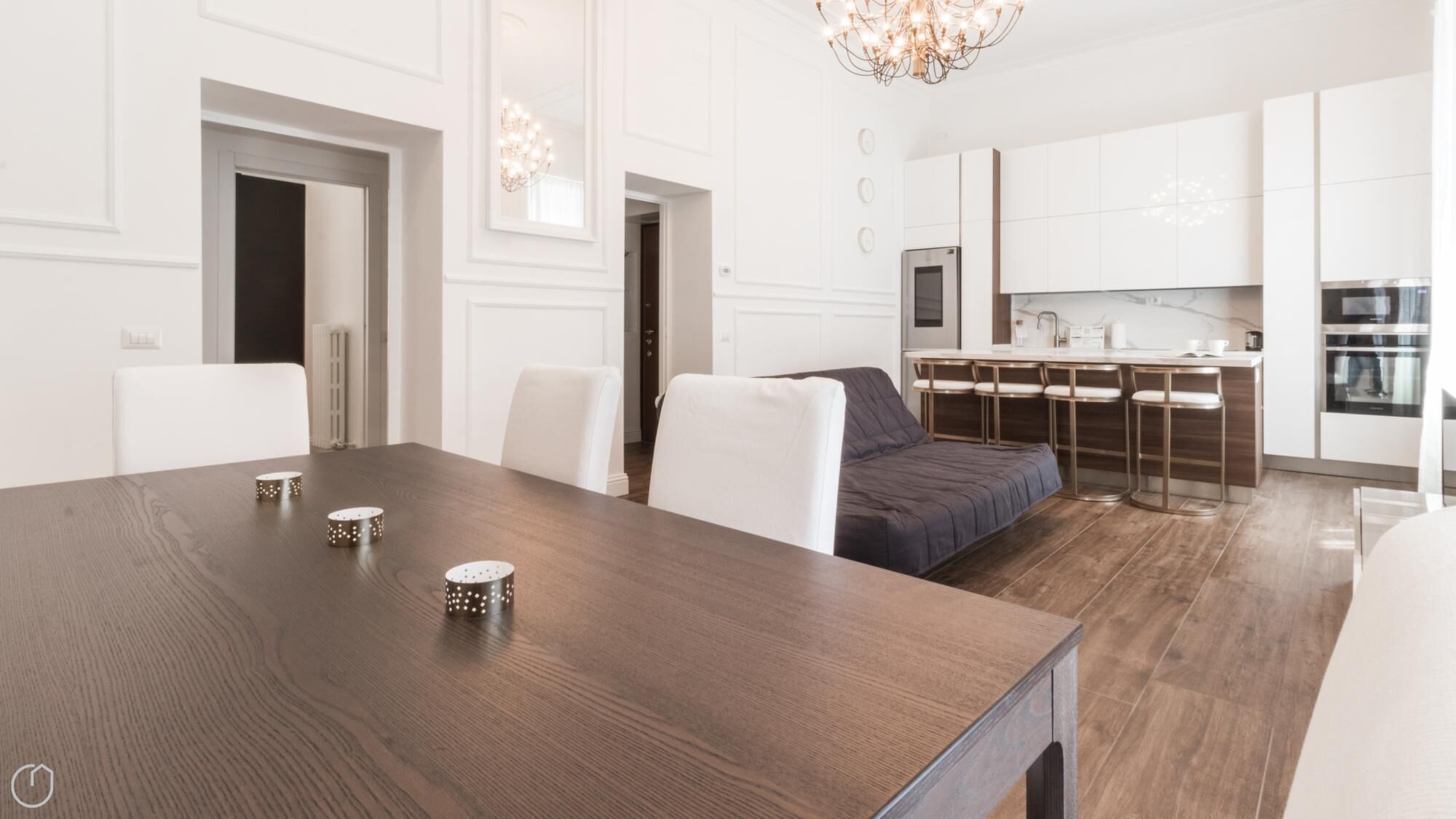 Eine moderne Küche mit weißen Schränken, ein Essbereich mit einem Holztisch und ein Bett mit dunkelblauer Bettdecke.