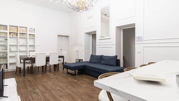 A modern, well-lit room with a sectional sofa, a dining table, and a bookshelf.