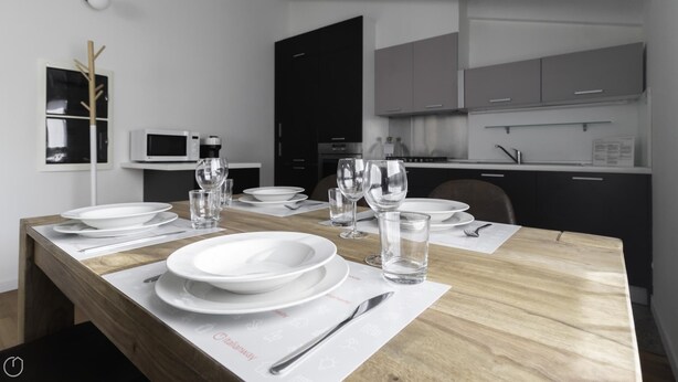 A modern dining area with a wooden table set for a meal, white plates, and clear glasses. - Italianway Comfort - Rubens 19 B (Milan)