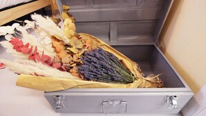 Een grijze metalen opbergdoos met een boeket gedroogde bloemen en bladeren.