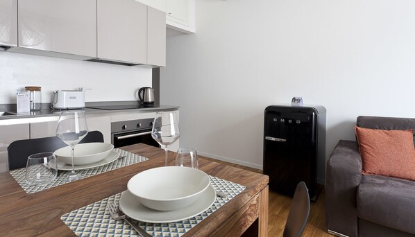 A modern kitchen with a dining table set for two, a coffee machine, and a compact refrigerator.