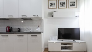 A modern kitchen with white cabinets, a black countertop, a red kettle, a toaster, and a Sony TV on a white stand. - Italianway Easy - Segrino 6 (Milan)