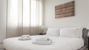 A neatly made bed with white linens and towels, a bedside lamp, and a decorative wall piece. - Italianway Easy - Segrino 6 (Milan)