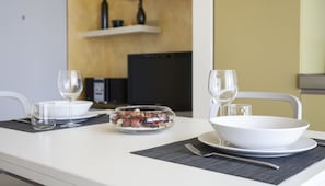 Une table à manger dressée avec de l’assiette blanche, des bols et des verres, et un saladier en verre transparent contenant des noix et des fruits secs.