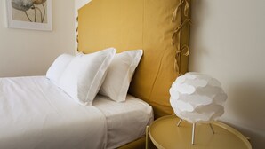 A bed with white bedding and two pillows, a mustard-colored headboard, and a round table with a white spherical object on it. - Italianway Comfort - Spadolini 6 (Milan)