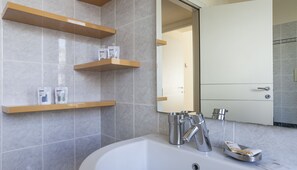 Une salle de bain moderne avec une baignoire, un miroir et trois étagères en bois où sont rangés les produits de toilette.