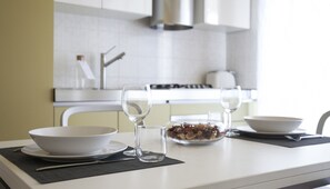 A modern kitchen with white cabinets, a stainless steel range hood, and a dining table set with a bowl, two wine glasses, and a glass of water. - Italianway Comfort - Spadolini 6 (Milan)