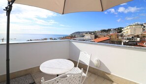 Un balcon avec une table et une chaise, donnant sur un paysage urbain côtier avec des bâtiments et une plage.