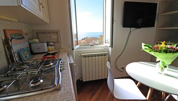 A kitchen with a gas stove, a toaster, and a window with a view of buildings and the sea.