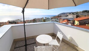 Un balcon avec une table et des chaises, offrant une vue sur le paysage urbain de la côte, avec ses bâtiments et la mer.