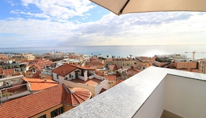 Un paisaje urbano costero con edificios de tejados terracota, cielo despejado y vista al mar.
