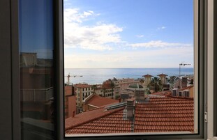 A view from a window overlooking a coastal cityscape with buildings, a clear sky, and the sea.