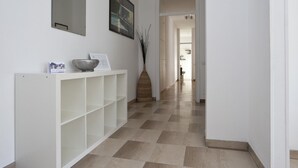 Un couloir avec une console blanche, un vase décoratif et un sol à carreaux.