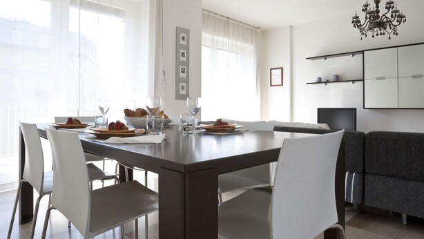 Un espace de salle à manger moderne avec une grande table, des chaises blanches et un canapé gris.