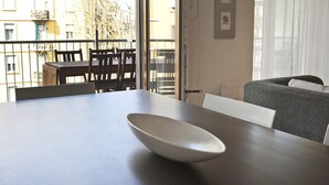 Une pièce moderne et minimaliste, dotée d’une grande table, d’un canapé et d’un balcon avec des chaises en bois.