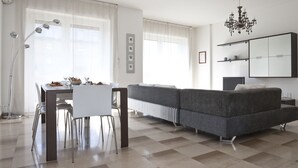 Un salon moderne avec un canapé gris, une table à manger avec des chaises, un lampadaire et un lustre.