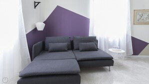 A modern room with a sectional sofa, a small round table, and a geometric wall design. - Italianway Easy - Argonne 39 (Milan)