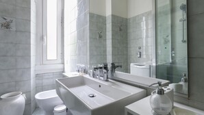 A modern bathroom with a large sink, a toilet, and a bidet. It features a large mirror and a shower area. - Italianway Easy - Argonne 39 (Milan)