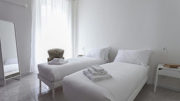 A hotel room with two beds, a chair, a nightstand, and a mirror. - Italianway Easy - Argonne 39 (Milan)