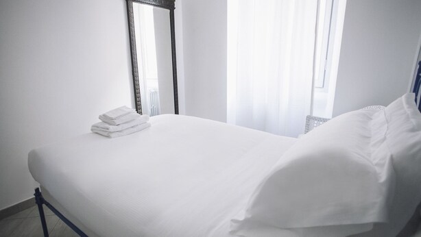A neatly made bed with white linens and pillows, a stack of folded towels, and a mirror on the wall. - Italianway Easy - Corso Sempione 96 (Milan)