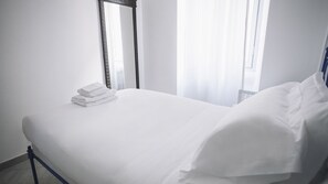 A neatly made bed with white linens and pillows, a stack of folded towels, and a mirror on the wall. - Italianway Easy - Corso Sempione 96 (Milan)