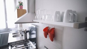A kitchen with white cabinets, a window with a plant, and a shelf with white mugs and glasses. - Italianway Easy - Corso Sempione 96 (Milan)