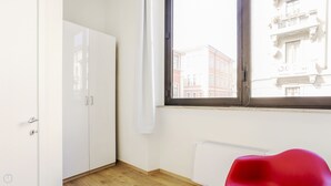 Una habitación con un armario blanco, un radiador y una ventana con vistas a edificios.