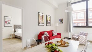 Una sala de estar moderna con un sofá rojo, sillas transparentes, una mesa de comedor con una bandeja de flores y obras de arte enmarcadas en las paredes.