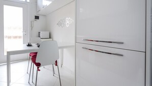 A modern kitchen with white cabinets, a microwave, and a dining area with a white chair and table. - Italianway Easy - Lambertenghi 3 (Milan)