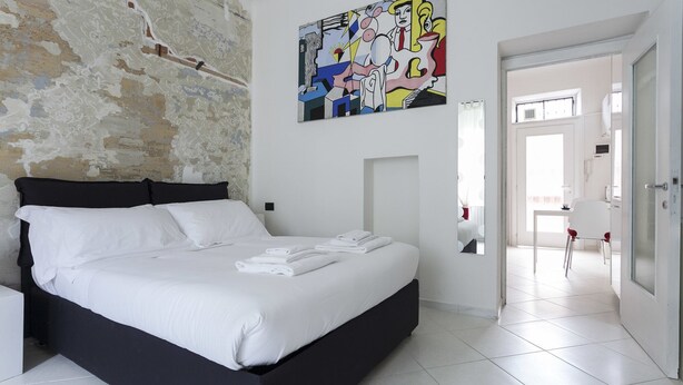 A modern bedroom with a large bed, a white wall with a textured pattern, and a colorful abstract painting above the bed. - Italianway Easy - Lambertenghi 3 (Milan)