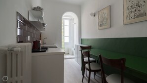 A modern kitchen with a white countertop, a red kettle, and a green bench.