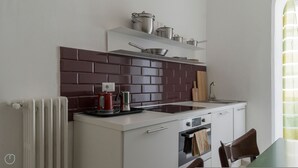 A compact kitchen with a white countertop, a red kettle, a stove, and a brick backsplash.