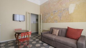 A living room with a sofa, a red chair, a small table, and a TV on the wall. - Italianway Easy - Melzo 12 - Vintage (Milan)