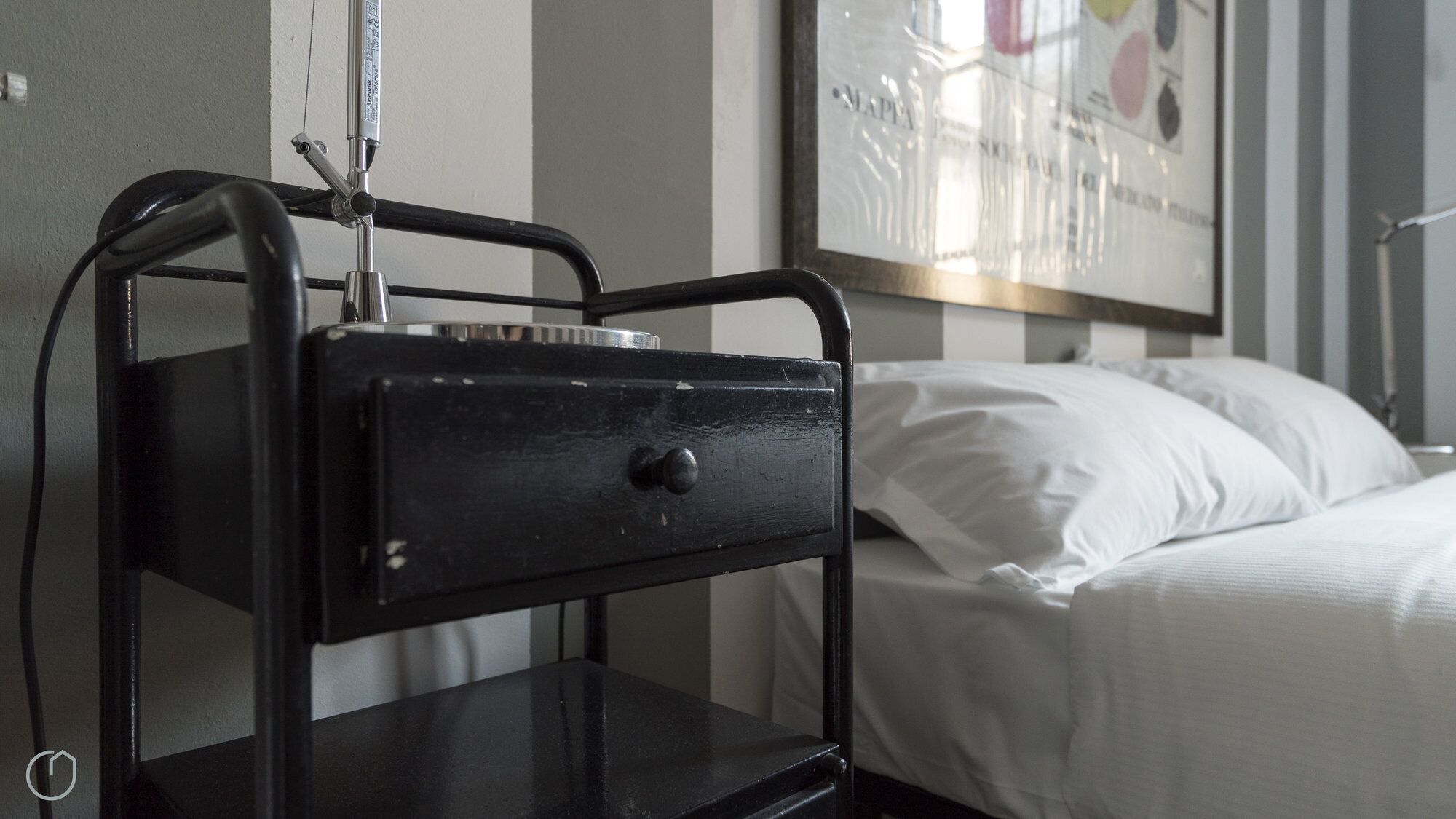 A bed with white linens and a black metal bedside table with a drawer.