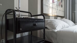 A bed with white linens and a black metal bedside table with a drawer.